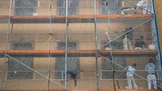 Arbeiter auf einem Baugerüst verrichten Arbeiten an der Fassade eines Hauses.