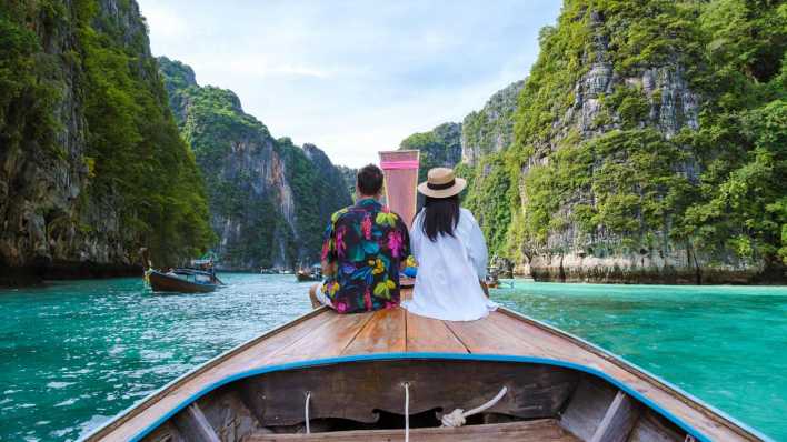 Ein Pärchen sitzt auf einem Longtail Boat in Thailand und fährt auf Maya Bucht der Insel Koh Phi Phi Leh ein (Bild: picture alliance / Zoonar )