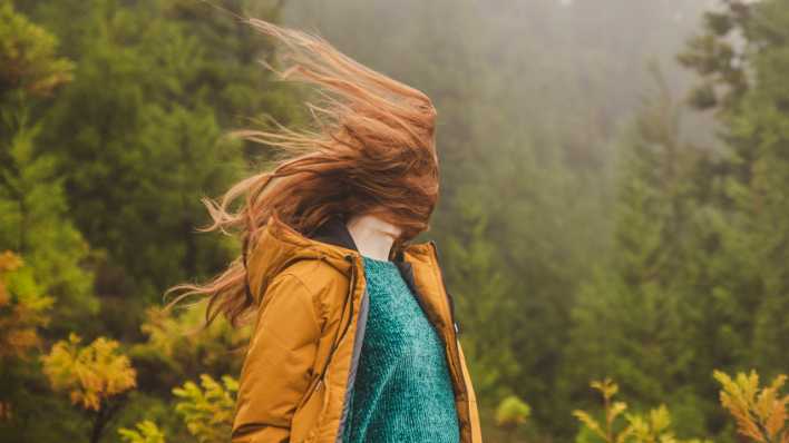 Frau mit langen roten Haaren steht im Wind