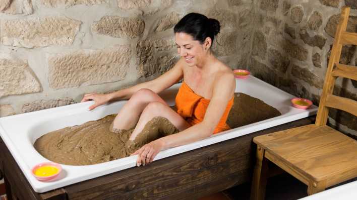 Frau sitzt in einer Wanne mit Heilerde