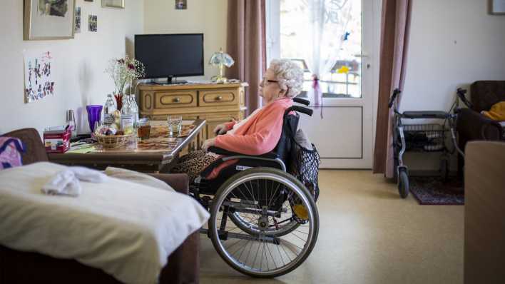 Eine aeltere Frau im Rollstuhl sitzt in ihrem Zimmer in einer Pflegeeinrichtung.