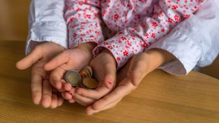 Ein Kind hält Münzen in seinen Händen und wird dabei von der Mutter unterstützt.