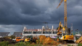 In einem Neubaugebiet stehen Kräne und Bagger an einem Wohnungsbauprojekt.