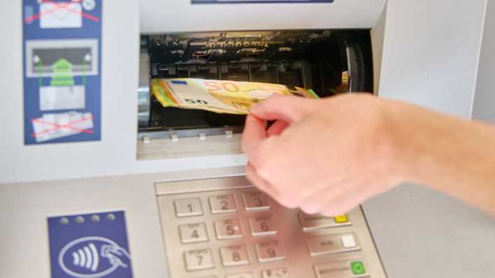 Eine Person legt Bargeld in einen Geldautomat