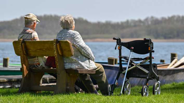 Symbolfoto Rente: Ein älteres Paar sitzt auf einer Bank am Ufer eines Sees