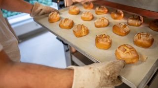 Eine Person schiebt in der Bäcker-Innung Berlin Blech mit Brötchen in den Ofen.
