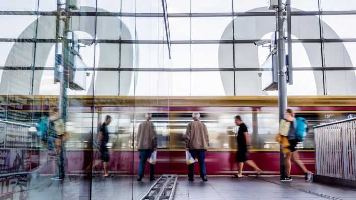 Eine S-Bahn fährt am Berliner Bahnhof Ostkreuz ein und spiegelt sich in Glasscheibe.