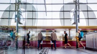 Eine S-Bahn fährt am Berliner Bahnhof Ostkreuz ein und spiegelt sich in Glasscheibe.
