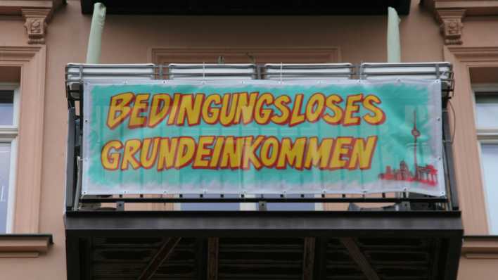 Ein Plakat, das am Balkon einer Wohnung in Berlin befestigt ist, wirbt für die Auszahlung eines staatlichen Grundeinkommens (Bild: picture alliance/ dpa)
