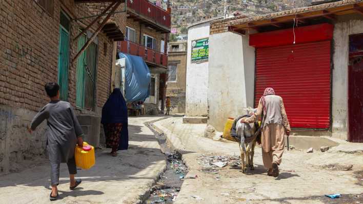 Menschen tragen Wasserbehälter in den Straßen von Kabul (Hauptstadt in Afghansitan (Bild: picture alliance))