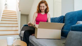 Symbolfoto Online-Shopping: Eine junge Frau packt ein Paket aus