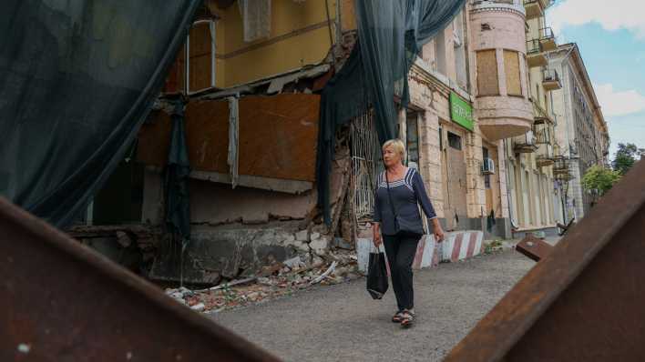Eine Einwohnerin von Kharkiv geht im Stadtzentrum an einem durch Bomben zerstörten Wohnhaus vorbei (Bild: picture alliance / Sofiia Bobok)