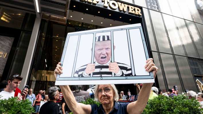 Eine Demonstrantin hält vor dem Trump Tower ein Plakat hoch, auf dem eine Karikatur von Donald Trump hinter Gittern zu sehen ist.