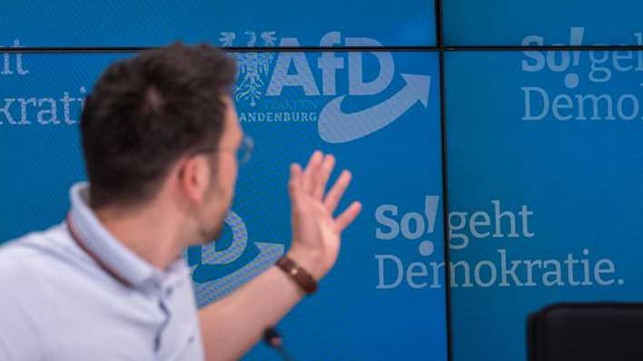 Dennis Hohloch, Parlamentarischer Geschäftsführer der AfD-Fraktion im Landtag von Brandenburg, deutet während einer Pressekonferenz auf den Slogan "So! geht Demokratie".