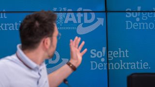 Dennis Hohloch, Parlamentarischer Geschäftsführer der AfD-Fraktion im Landtag von Brandenburg, deutet während einer Pressekonferenz auf den Slogan "So! geht Demokratie".