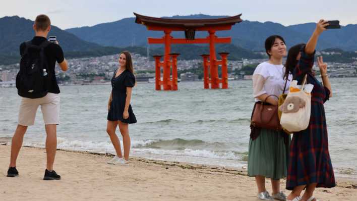 Junge Menschen machen Handy-Fotos vor dem Itsukushima-Schrein, ein Unesco-Weltkulturerbe in Japan.