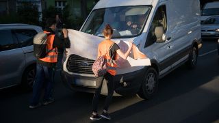 Aktivisten und Aktivistinnen blockieren während einer Laufblockade der Klimaschutzgruppe Letzte Generation auf der Bornholmer Straße in Berlin ein Auto.