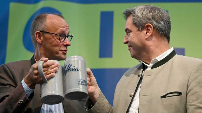 Friedrich Merz (l), Bundesvorsitzender der CDU, und Markus Söder (CSU), Ministerpräsident von Bayern, stoßen beim Politischen Frühschoppen Gillamoos auf der Bühne mit Bierkrügen an.
