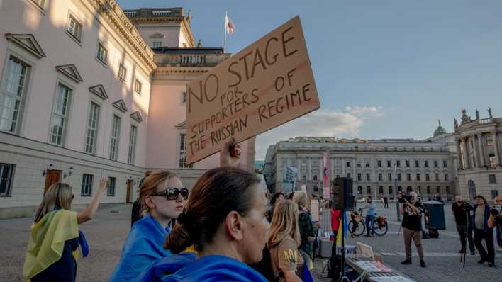 Eine Frau hält vor der Staatsoper Berlin ein Schild mit der Aufschrift "No stage for supports of the Russian regime" hoch, als Protest gegen den Auftritt von Anna Netrebko.