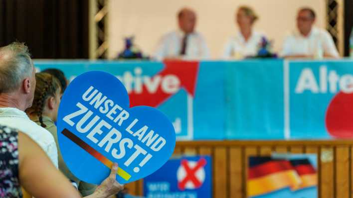 Eine AfD-Anhängerin hält ein Schild in Herzform "Unser Land zuerst!" hoch.