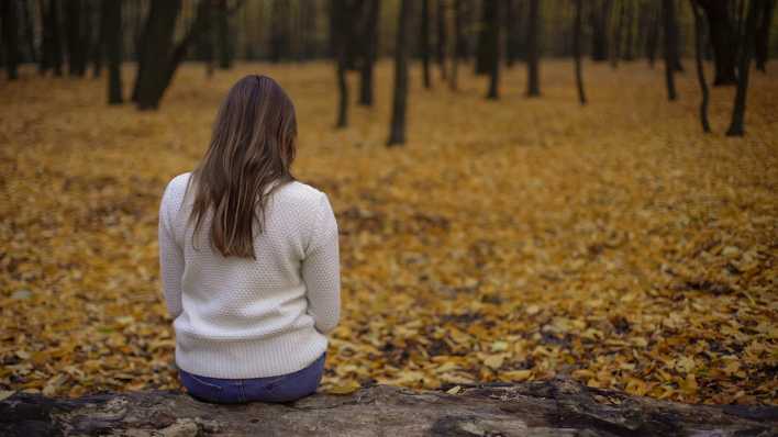 Eine Frau sitzt allein in einem herbstlichen Park.
