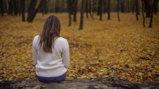 Eine Frau sitzt allein in einem herbstlichen Park.