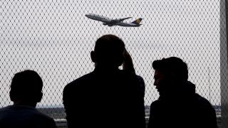 Eine Familie schaut einem startenden Flugzeug durch ein Gitter hinterher.