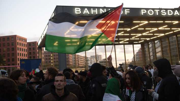Menschchen stehen bei einer verbotenen Pro-Palästina-Demonstratin am Potsdamer Platz. Eine Frau hält dabei eine Palästinenser-Fahne. (Bild: picture alliance/dpa | Paul Zinken)