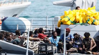 Gerettete Migranten sitzen auf einem Boot der italienischen Finanzpolizei, bevor sie im Hafen der sizilianischen Insel Lampedusa von Bord gehen (Bild: picture alliance / Cecilia Fabiano)