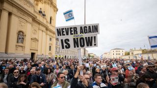 Ein Teilnehmer der Kundgebung "Solidarität mit Israel - Gegen gegen Terror, Hass und Antisemitismus" hält ein Schild mit der Aufschrift "NEVER AGAIN IS NOW!" in die Höhe.