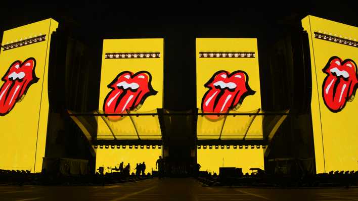 Ein Bühnbild der Rolling Stones zeigt vier herausgestreckte Zungen, das Markenzeichen der Band (Bild: dpa / Carsten Rehder)