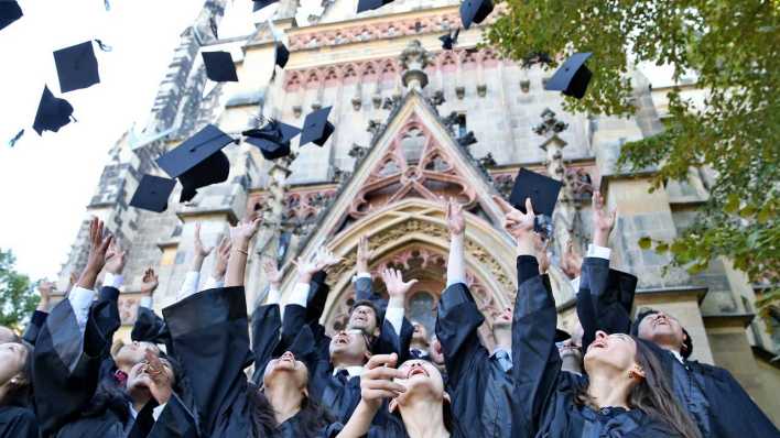 ARCHIV: Absolventen werfen ihre Doktorhüte vor der Thomaskirche in Leipzig in die Luft (Bild: picture alliance / dpa)