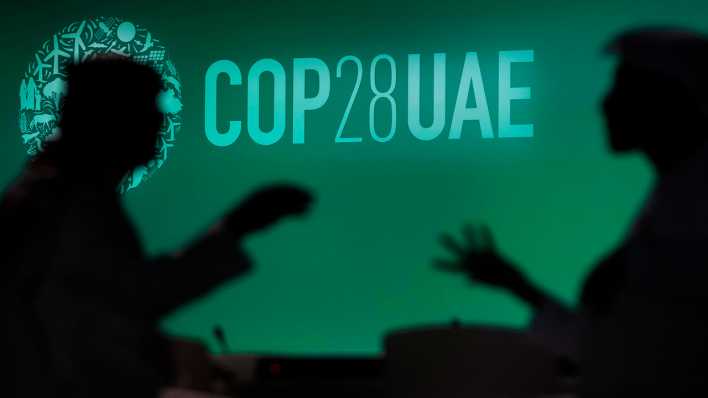 Zwei Menschen unterhalten sich vor einem Logo des UN-Klimagipfels COP28.