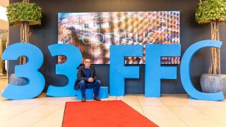 Bernd Buder, Programmdirektor des Filmfestivals Cottbus, sitzt in einem Einkaufszentrum vor dem aus Kunststoff gebildeten Schriftzug «33. FFC»