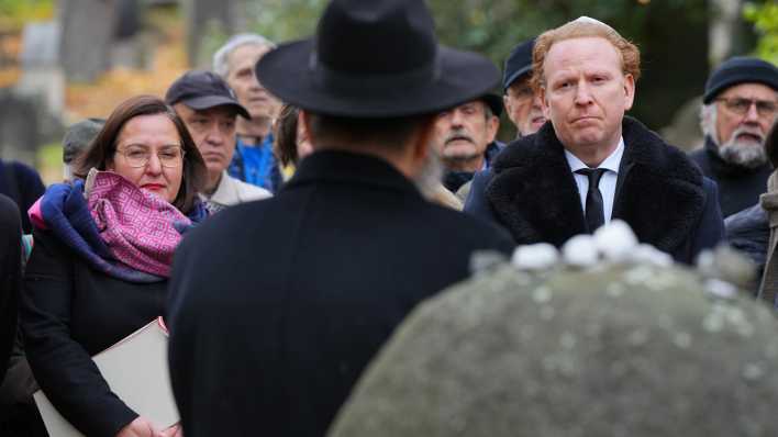 Manja Schüle (SPD) und der irisch-deutsche Geiger Daniel Hope verfolgen auf dem Jüdischen Friedhof während einer Gedenkveranstaltung zum 85. Jahrestag der Pogromnacht die Rede des Landesrabbiners.