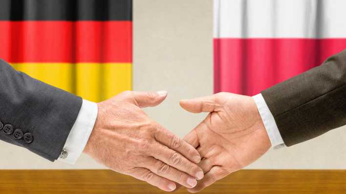 Zwei Männer reichen sich die Hand. Im Hintergrund sind eine Deutschland- und eine Polenfahne zu sehen (Bild: Zerbor/Shotshop/picture alliance)