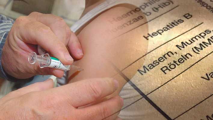 Ein Kind wird gegen Masern geimpft. Im Hintergrund sind Einträge aus einem Impfbuch zu sehen. (Bild: picture alliance / SvenSimon)s