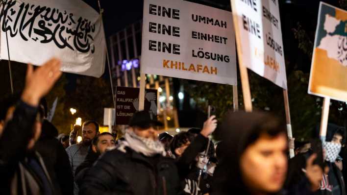 Kundgebung "Gaza unter Beschuss - gemeinsam gegen das Unrecht", darunter ein Plakat mit Schriftzug "Eine Ummah - eine Einheit - eine Lösung - Khilafah" (Bild: picture alliance/dpa)