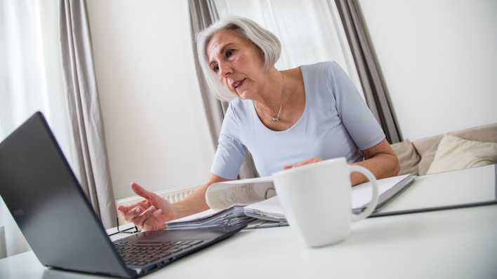 Eine ältere Frau sitzt am einem Tisch und arbeitet mit Papierunterlagen und Kaffeee am Laptop (Bild: picture alliance / dpa Themendienst | Christin Klose) Eine ältere Frau sitzt am einem Tisch und arbeitet mit Papierunterlagen und Kaffeee am Laptop (Bild: picture alliance / dpa Themendienst | Christin Klose)
