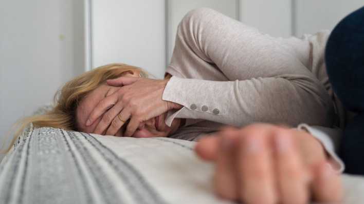 Frau in den Wechseljahren liegt deprimiert auf einem Bett