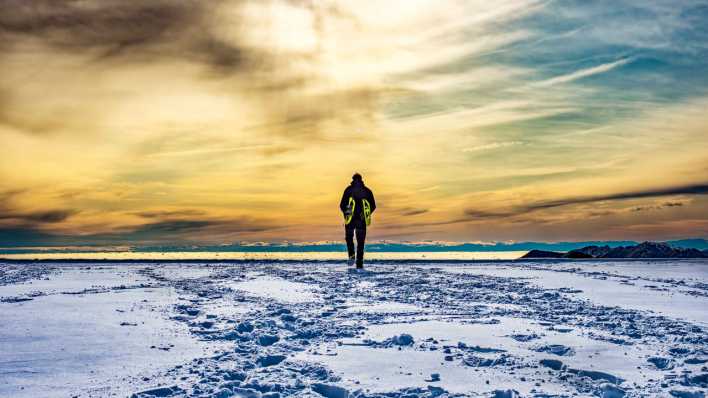Mann wandert auf Schnee in den Sonnenuntergang