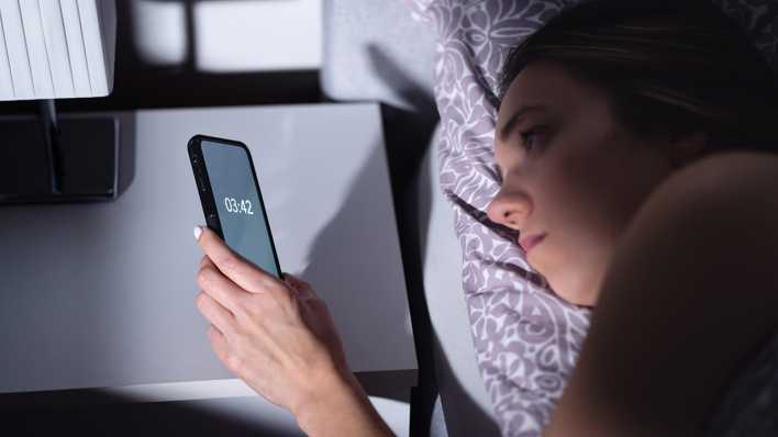 Eine Frau liegt im Bett und schaut um 3:42 Uhr auf ihr Handy.