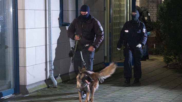 Polizisten mit einem Hund gehen zu einem Haus. Die Bundesanwaltschaft hat in Berlin und im niederländischen Rotterdam vier mutmaßliche Mitglieder der islamistischen Hamas festnehmen lassen.