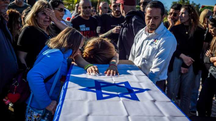 Familie und Freunde trauern während einer Beerdigung, auf dem Sarg liegt eine israelische Flagge.