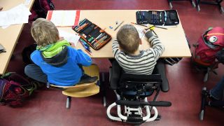 Ein Kind sitzt in seinem Rollstuhl mit einem anderen Schüler im Klassenzimmer