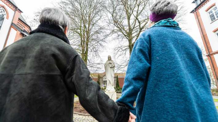 Hand in Hand stehen zwei Frauen an einem Kloster vor einer Maria-Statue. (Bild: picture alliance/dpa | Guido Kirchner)