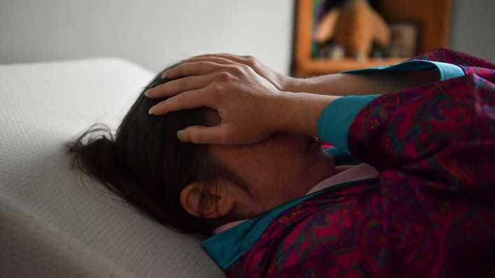 Eine Patientin, die seit 2020 an Long Covid leidet, liegt im Bett und hält die Hände vors Gesicht.