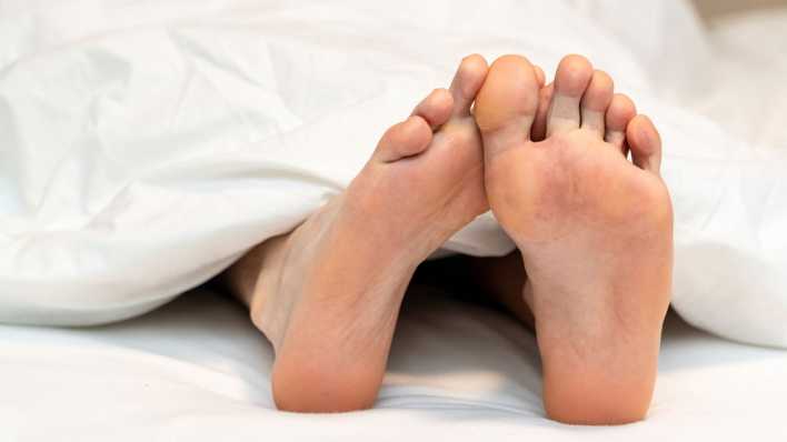 Füße eines kranken Mannes schauen unter der Bettdecke hervor