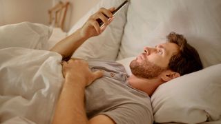Mann liegt mit Handy im Bett