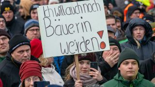 Eine junge Frau hält auf einer Kundgebung ein Schild mit der Aufschrift "Ich will auch noch Bäuerin werden!" hoch.